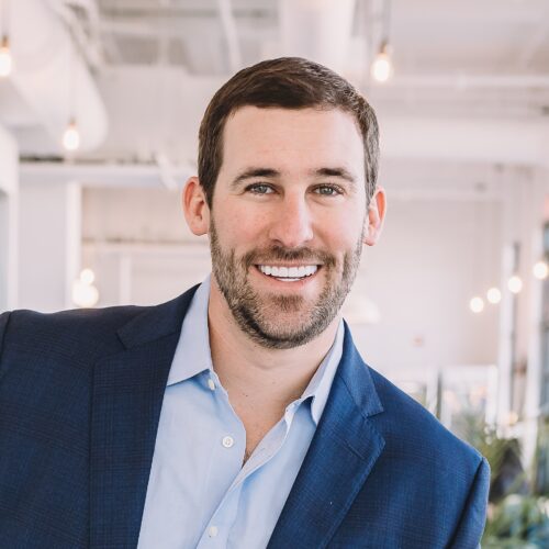 Man in a suit smiling in a modern office setting.