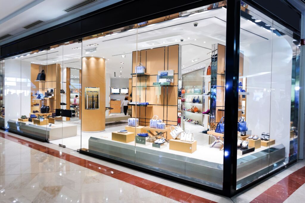 Step into our luxury retail store, where handbags, shoes, and accessories are elegantly displayed on shelves and pedestals within a brightly lit interior. Discover a world of style that could redefine your wardrobe as if embarking on a Courseon fashion mastery.