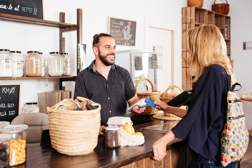 Smiling Cashier Accepts Credit Card From Customer at Grocery Checkout Counter